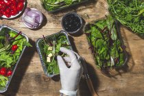 Top view crop anonymous chef in glove adding black olives to mix leaves salad with butter cubes — Photo de stock