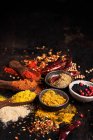 Spezie aromatiche colorate assortite in ciotole e cucchiai di legno disposti su tavolo scuro con condimenti sparsi — Foto stock