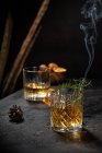 Vaso de cristal de bebida de whisky a la antigua adornado con romero fresco y cáscara de naranja en la mesa negra - foto de stock