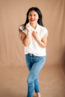 Satisfied ethnic female in casual outfit with toothy smile looking away while standing on brown background in studio — Fotografia de Stock