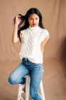 Satisfied ethnic female in casual outfit with toothy smile looking away while standing on brown background in studio — Fotografia de Stock