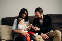 Giovane padre che gioca con adorabile piccolo figlio seduto sulle ginocchia di madre etnica con giocattolo in legno in mano — Foto stock
