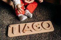Kleines, unkenntlich gemachtes Baby spielt auf dem Boden mit Holzspielzeug mit Tiago-Namensbuchstaben — Stockfoto