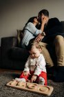 Unerkennbare junge Eltern küssen sich auf Sofa neben entzückendem kleinen Sohn, der auf dem Boden mit Holzspielzeug mit Tiago-Namensbuchstaben spielt — Stockfoto