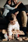 Unerkennbare junge Eltern umarmen sich auf Sofa neben entzückendem kleinen Sohn, der auf dem Boden mit Holzspielzeugbuchstaben spielt — Stockfoto
