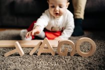 Привабливе маля бавиться на підлозі з дерев'яною іграшкою з листами з Тяго. — стокове фото