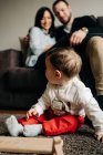 Невпізнавані молоді батьки обіймають один одного на дивані біля чарівного маленького сина, який грає на підлозі з дерев'яними іграшковими літерами — стокове фото