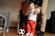Piccolo ragazzo calci palla mentre gioca con il padre irriconoscibile ritagliato a casa — Foto stock