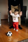 Маленький мальчик пинает мяч, играя с обрезанным неузнаваемым отцом дома — стоковое фото