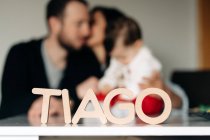 Nome della lettera Tiago in legno posta sul tavolo vicino a un giovane genitore irriconoscibile che bacia e abbraccia il bambino — Foto stock