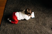 Зверху вміст маленький хлопчик лежить на пухнастому килимі і дивиться смішне відео на мобільний телефон у світлій вітальні — стокове фото
