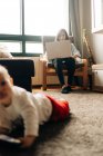 Content little baby boy lying on fluffy carpet and watching funny video on mobile phone in light living room — Fotografia de Stock