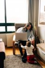Contento joven madre sentado en cómodo silla y navegación netbook cerca adorable pequeño hijo - foto de stock