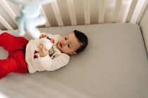 Сверху очаровательный маленький мальчик лежит в удобной кроватке и играет с белой резиновой туфлей — стоковое фото