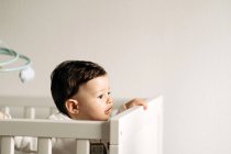 From above adorable little boy standing in comfy crib looking away — Photo de stock