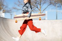 Вид сбоку на обрезанную неузнаваемую счастливую молодую женщину в стильной одежде, прыгающую на бетонном скейт-парке — стоковое фото