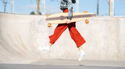 From below side view of cropped unrecognizable happy young female in stylish apparel jumping on concrete skate park — Photo de stock
