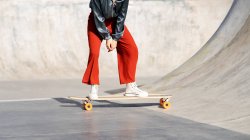 Crop anonymous female in stylish wear riding longboard during training in skate park — Stock Photo