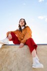 Niedriger Winkel einer Teenagerin in trendigen Klamotten und Gummischuhen, die von einem Betonzaun aus in die Kamera blickt — Stockfoto