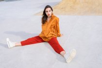 From above full body young female in stylish outfit sitting in concrete skate park while looking at camera in sunlight — Fotografia de Stock
