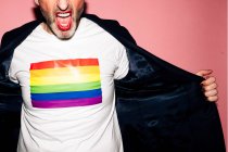 Ritagliato uomo barbuto fiducioso irriconoscibile con labbra rosse urlando e dimostrando bandiera LGBT su t shirt bianca su sfondo rosa — Foto stock