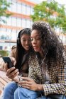 Asiatico femmina avendo divertente chiamata su smartphone e focalizzata nero donna ascoltare musica e navigazione internet su cellulare — Foto stock
