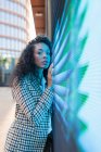 Wistful black female in casual clothes with curly hair looking at camera while leaning on wall with neon illumination — Fotografia de Stock