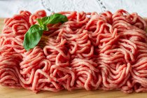 From above of fresh raw mixed pork and beef minced meat on wooden cutting board with green basil leaves placed on table during cooking process — Stock Photo
