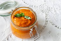 From above full glass jar with homemade natural tomato sauce garnished with fresh green basil leaves placed on table — Fotografia de Stock