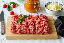 From above of fresh raw mixed pork and beef minced meat on wooden cutting board with green basil leaves placed on table during cooking process near homemade tomato sauce — Stock Photo