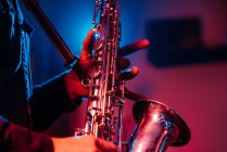 Crop безликий професійний музикант грає на саксофоні з пальцями на ключах під час живого концерту в неонових вогнях — стокове фото