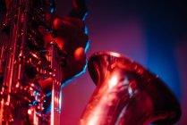 Crop faceless professional musician playing saxophone with fingers on keys during live concert in neon lights — Fotografia de Stock