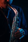Crop musician with playing saxophone in red and blue neon lights during live performance — Fotografia de Stock