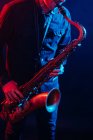 Профессиональный музыкант играет на саксофоне в красном и синем неоновом свете во время живого выступления — стоковое фото