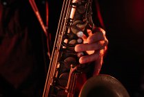 Crop músico profesional sin rostro tocando el saxofón con los dedos en las teclas durante el concierto en directo en luces de neón - foto de stock