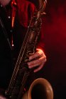 Crop faceless professional musician playing saxophone with fingers on keys during live concert in neon lights — Fotografia de Stock