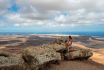 Wanderin in lässigem Outfit sitzt auf einem felsigen Hügel und genießt an klaren Tagen das weite hügelige Tal — Stockfoto