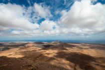 Живописный пейзаж бурного холмистого побережья у синего моря под голубым небом с пушистыми облаками — стоковое фото