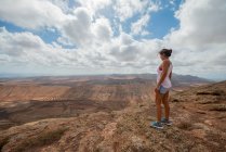 Eine Wanderin in lässigem Outfit steht auf einem felsigen Hügel und genießt an klaren Tagen das weite hügelige Tal — Stockfoto