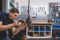 Seitenansicht des männlichen Mechanikers mit Schraubenzieher, der das Rad des Elektrorollers in der Werkstatt fixiert — Stockfoto