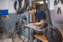 Вид сбоку мужчины с отверткой, закрепляющей колесо электроскутера в мастерской — стоковое фото