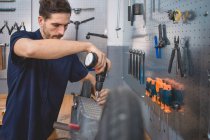 Опытный взрослый мастер-мужчина с помощью электрической отвертки при ремонте современного скутера в профессиональной мастерской — стоковое фото