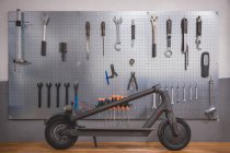 Incomplete electric scooter placed near wall with various repair tools and instruments in modern workshop — Fotografia de Stock