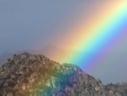 Vivid rainbow on cloudy sky over mountain ridge — Stock Photo