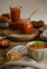 Повні скляні банки з домашнім натуральним смаженим томатним соусом розміщені на обробній дошці поруч зі свіжим зеленим розмарином і листям базиліка, розміщеним на сільському дерев'яному столі — стокове фото