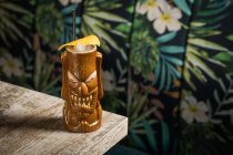 Braune skulpturale Tiki-Tasse mit Alkoholgetränk, dekoriert mit Stroh und Eis, platziert auf einem Tisch auf verschwommenem Hintergrund — Stockfoto
