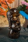 Brauner skulpturaler Tiki-Becher mit Alkoholgetränk, dekoriert mit Stroh und Eis auf dem Tisch — Stockfoto