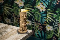Taza tiki escultórica tradicional de bebida alcohólica con paja colocada en una mesa de madera - foto de stock