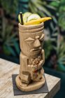 Copo tradicional de tiki escultural de bebida alcoólica com palha colocada na mesa de madeira — Fotografia de Stock