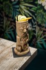 Tasse traditionnelle sculpturale tiki de boisson alcoolisée avec de la paille placée sur une table en bois — Photo de stock